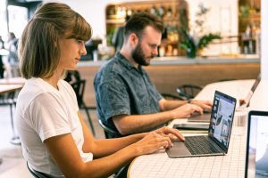 Two young professionals working on laptops in a modern cafe setting. — Advantages for Employers