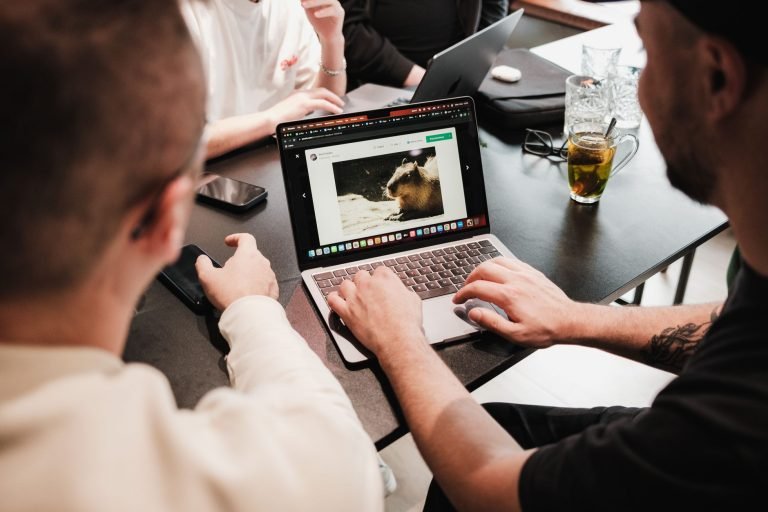 A group of men collaborating at a desk with laptops, showcasing teamwork and technology use in an office environment. — Why a